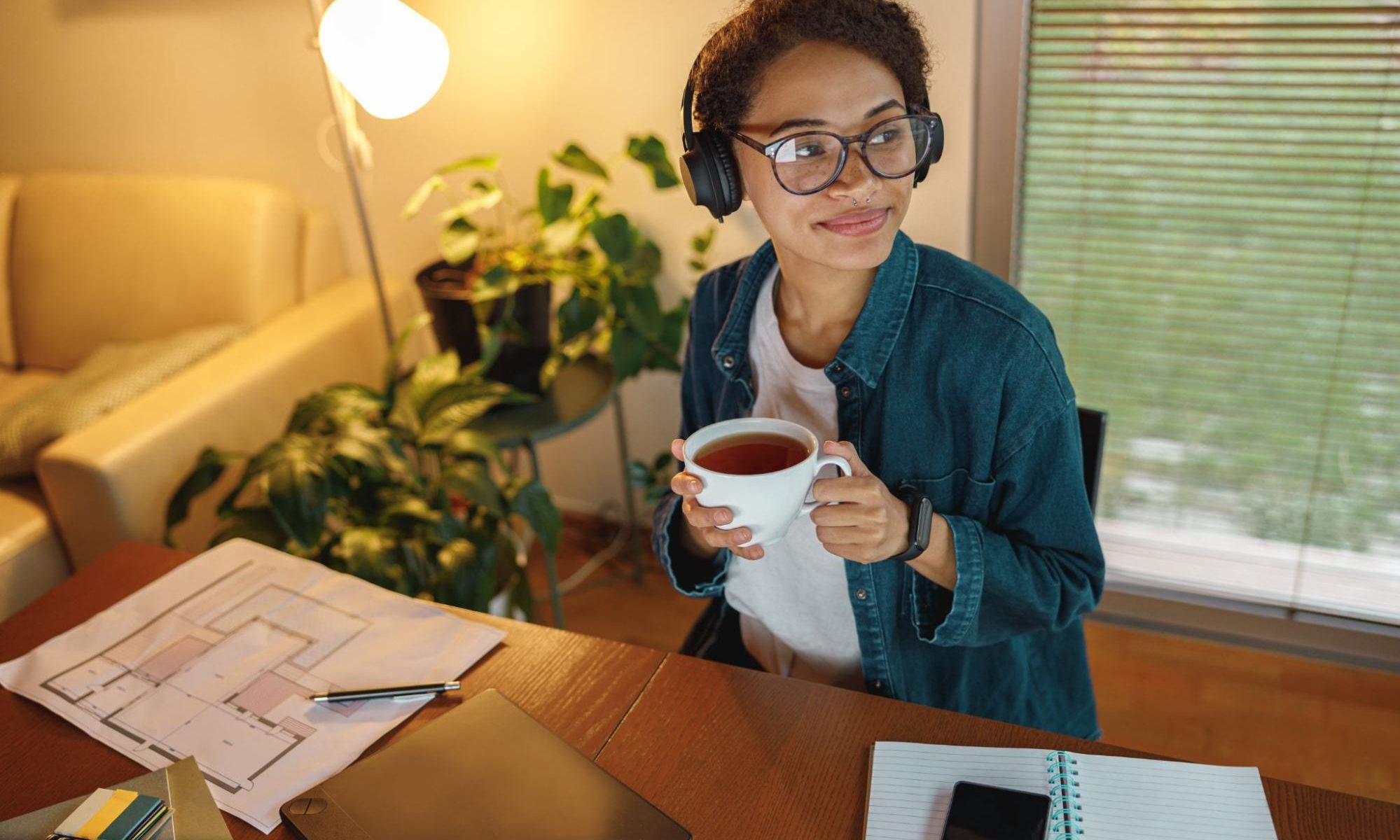 Professional working from home at a desk with laptop and plans, enjoying tea while managing flexible remote business tasks.